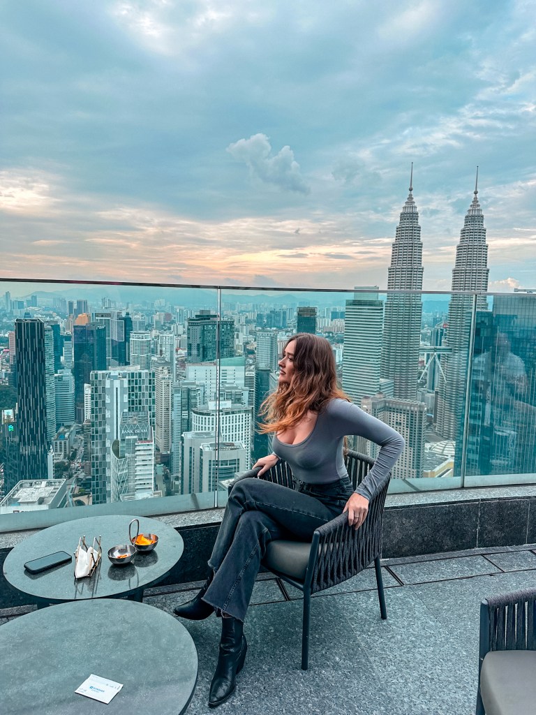 Carlijn de Jong sitting on a rooftop terrace overlooking the Kuala Lumpur skyline and Petronas Twin Towers
