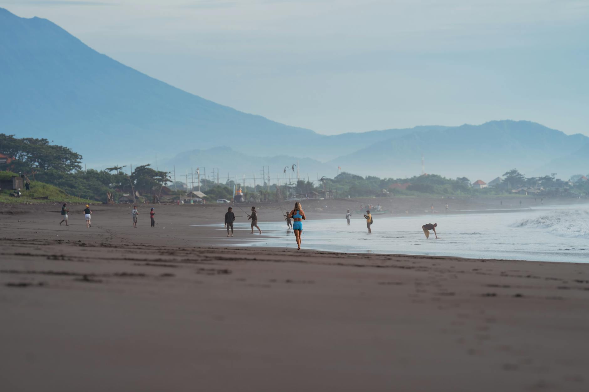 Woman walking along Sanur Beach with calm water and mountain views in Bali
