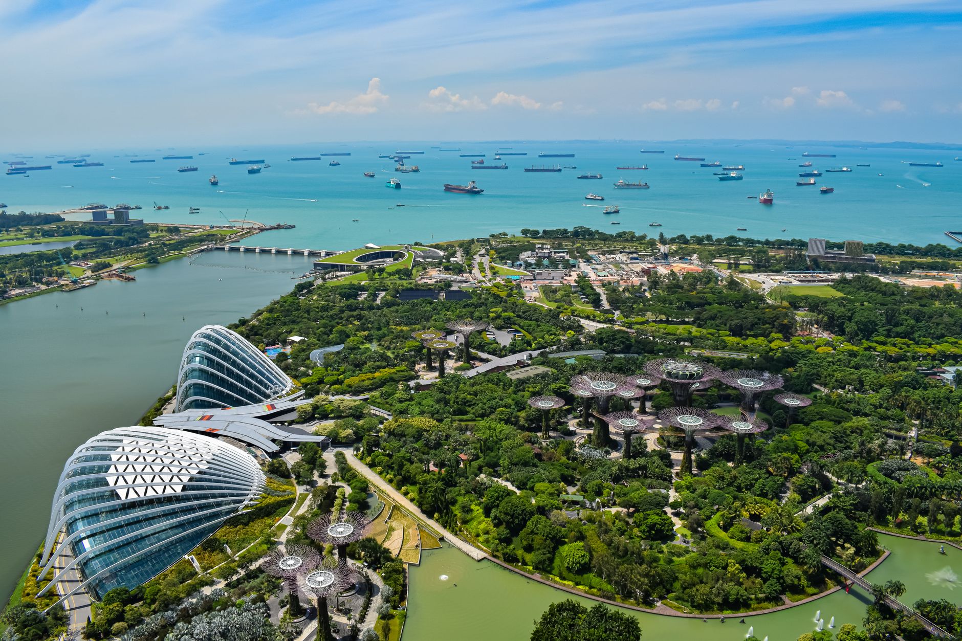 Aerial view over Gardens by the Bay, Marina Bay, and Singapore harbor with boats in the distance