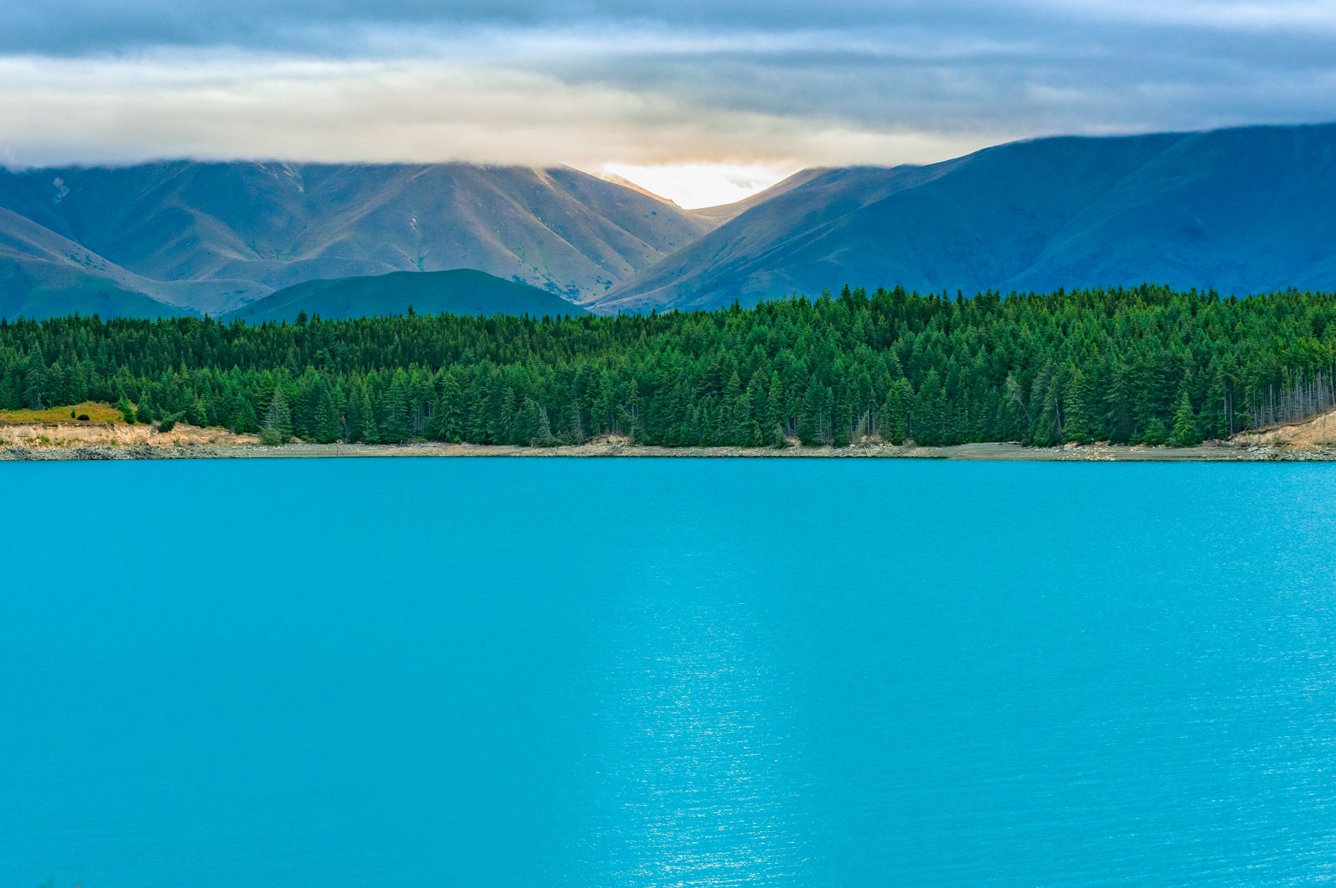 Bright blue lake surrounded by forest and mountains in New Zealand