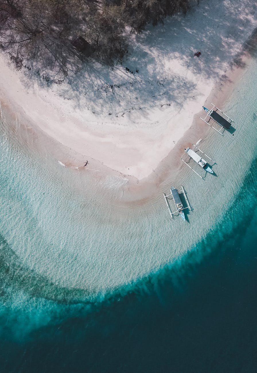 Aerial view of white sand beach and turquoise water in Bali with traditional boats on the shore