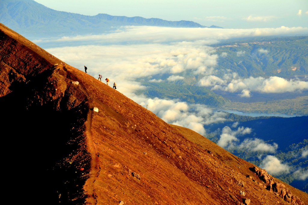 Hikers climbing the orange volcanic slope of Mount Agung
