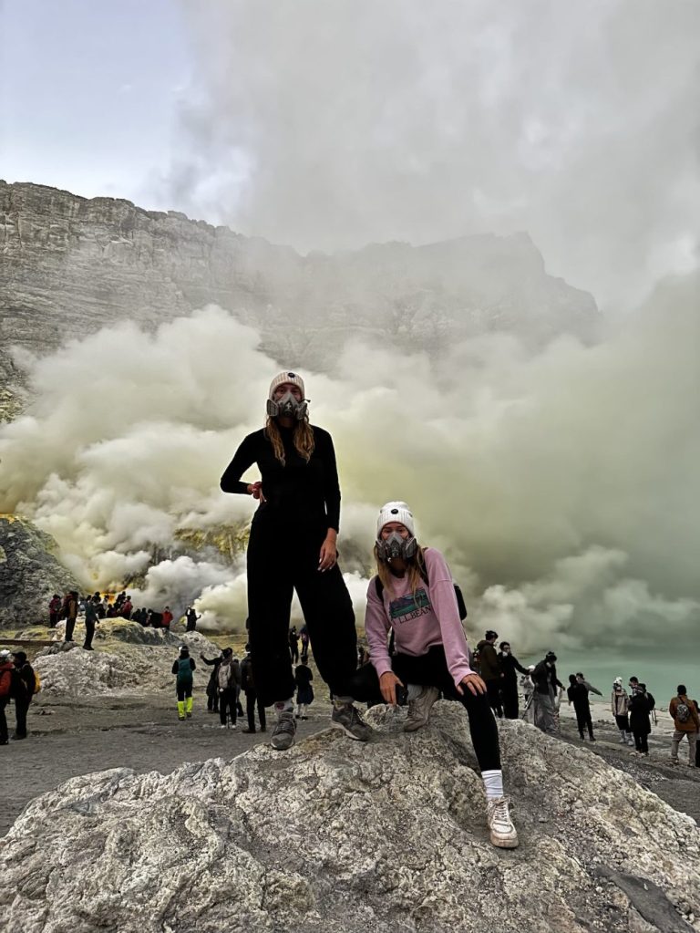 Travelers standing by Mount Ijen crater lake with huge sulfur plumes in the background during a volcano hike in Indonesia