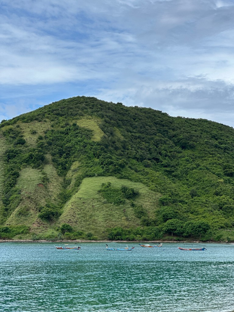 Mawun Beach in South Lombok with green hills, calm water, and fishing boats near the shore