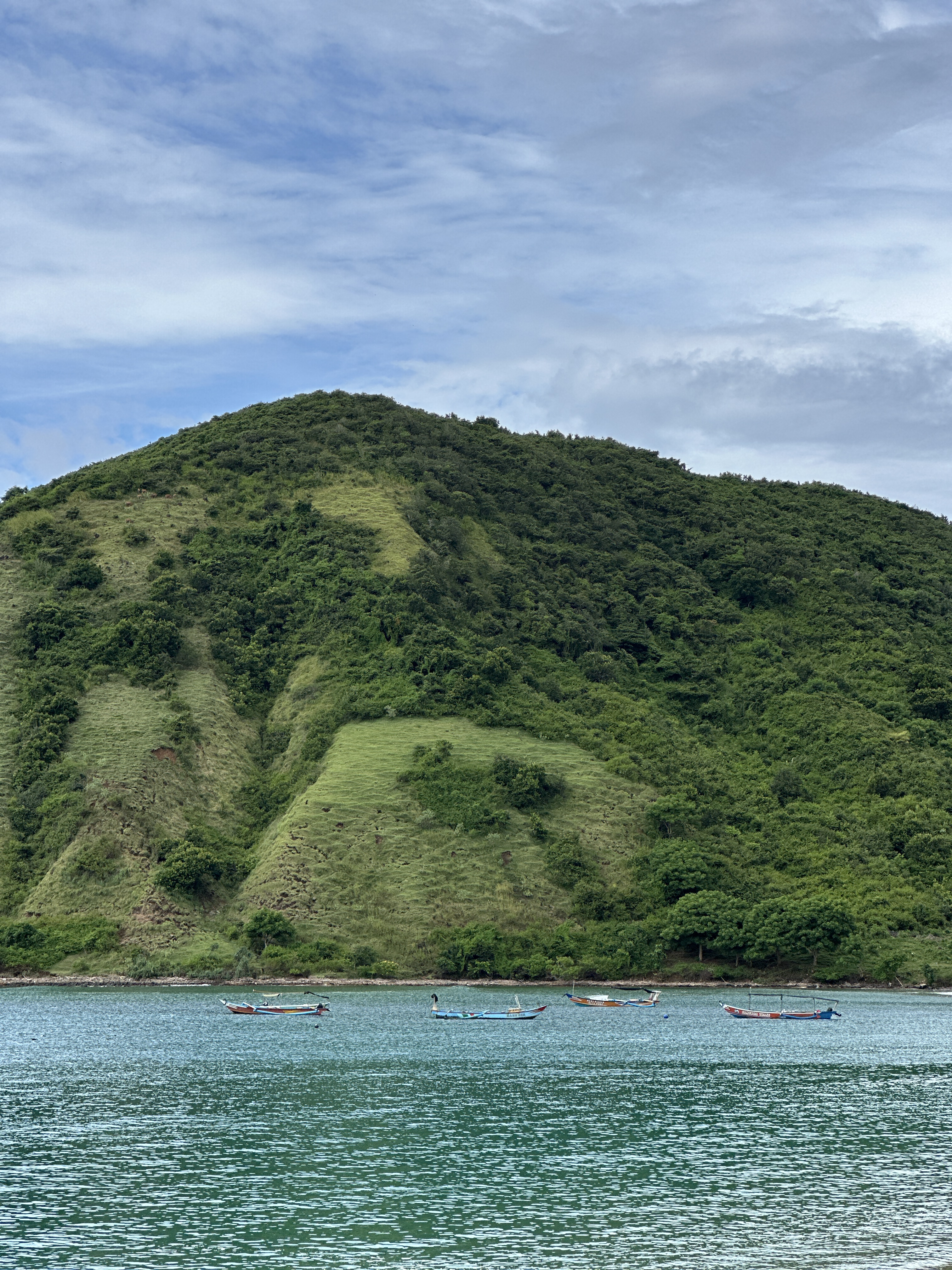 Mawun Beach in South Lombok with green hills, calm water, and fishing boats near the shore