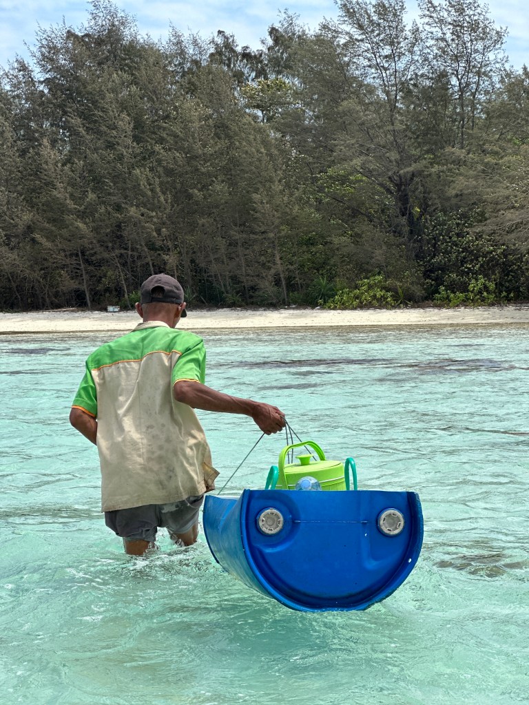 Local guide carrying snorkeling gear through shallow turquoise water near Gili Gede, Lombok