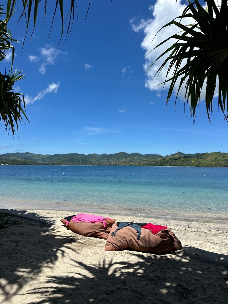 Quiet beach on Gili Asahan with clear turquoise water and beanbags under palm shade