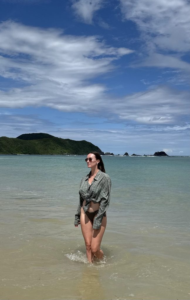 Quiet Lancing Beach in Lombok with clear water, green hills, and a woman standing in the sea