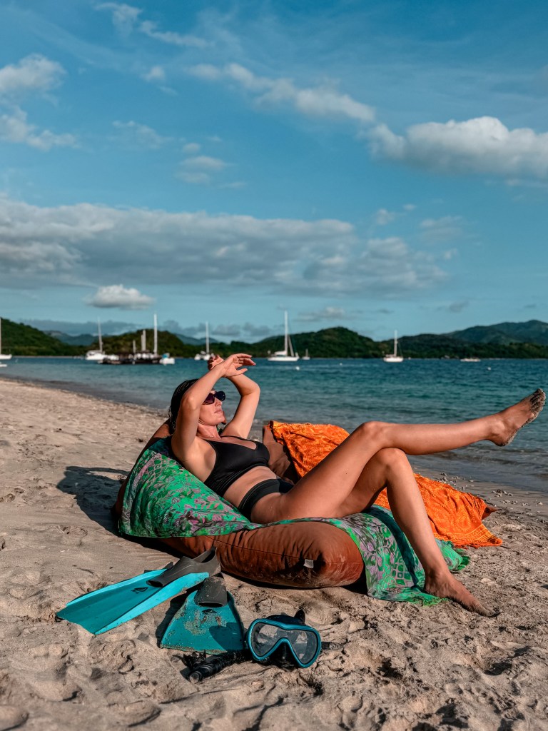 Relaxing on a beach in Lombok with snorkel gear and boats in the bay