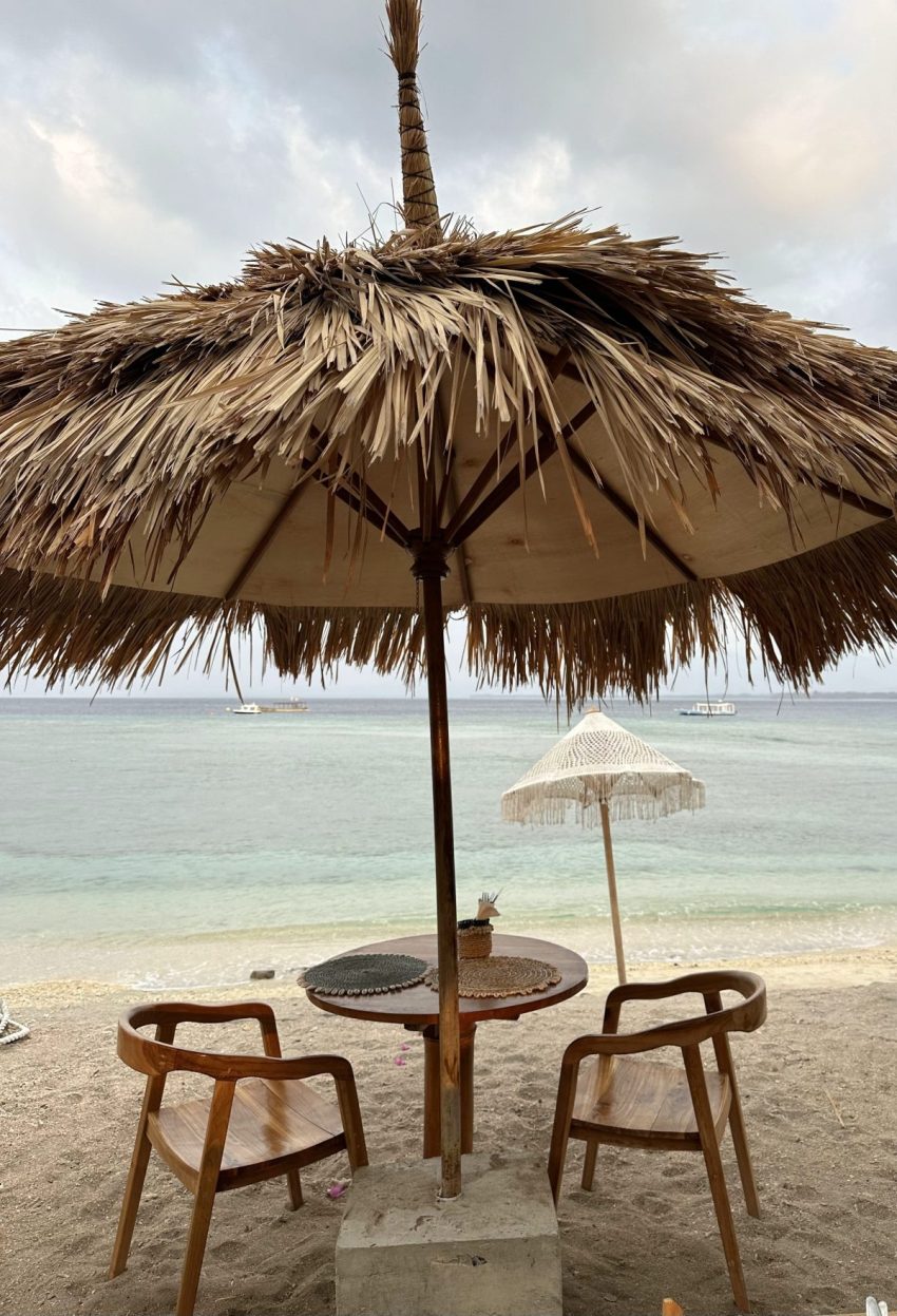 Beach cafe table under a straw umbrella overlooking the ocean on Gili Air, Indonesia