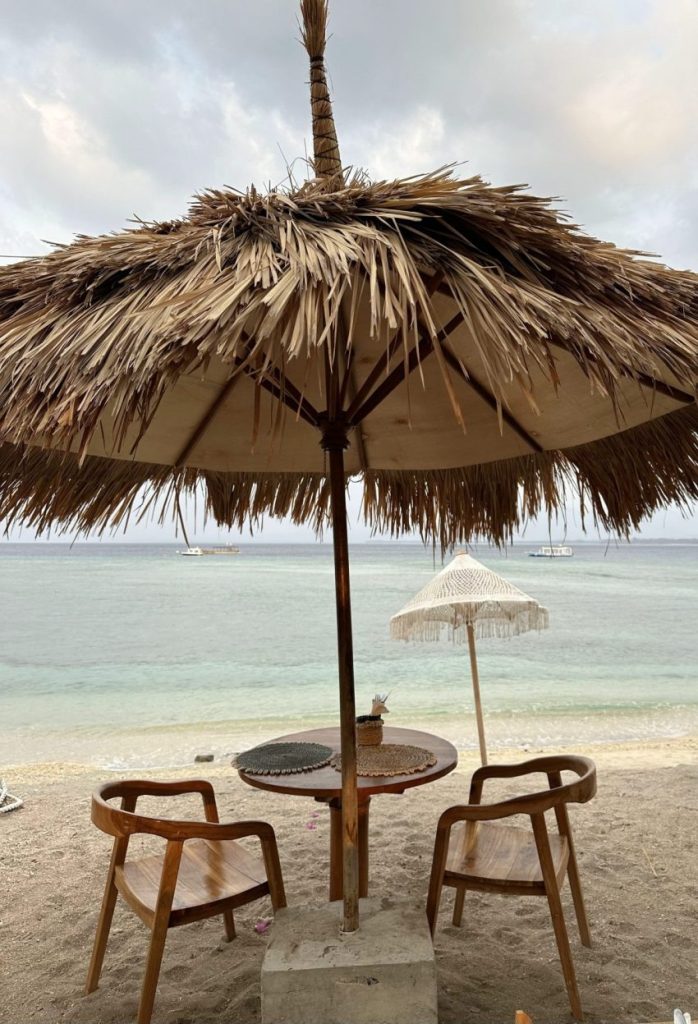 Beach cafe table under a straw umbrella overlooking the ocean on Gili Air, Indonesia
