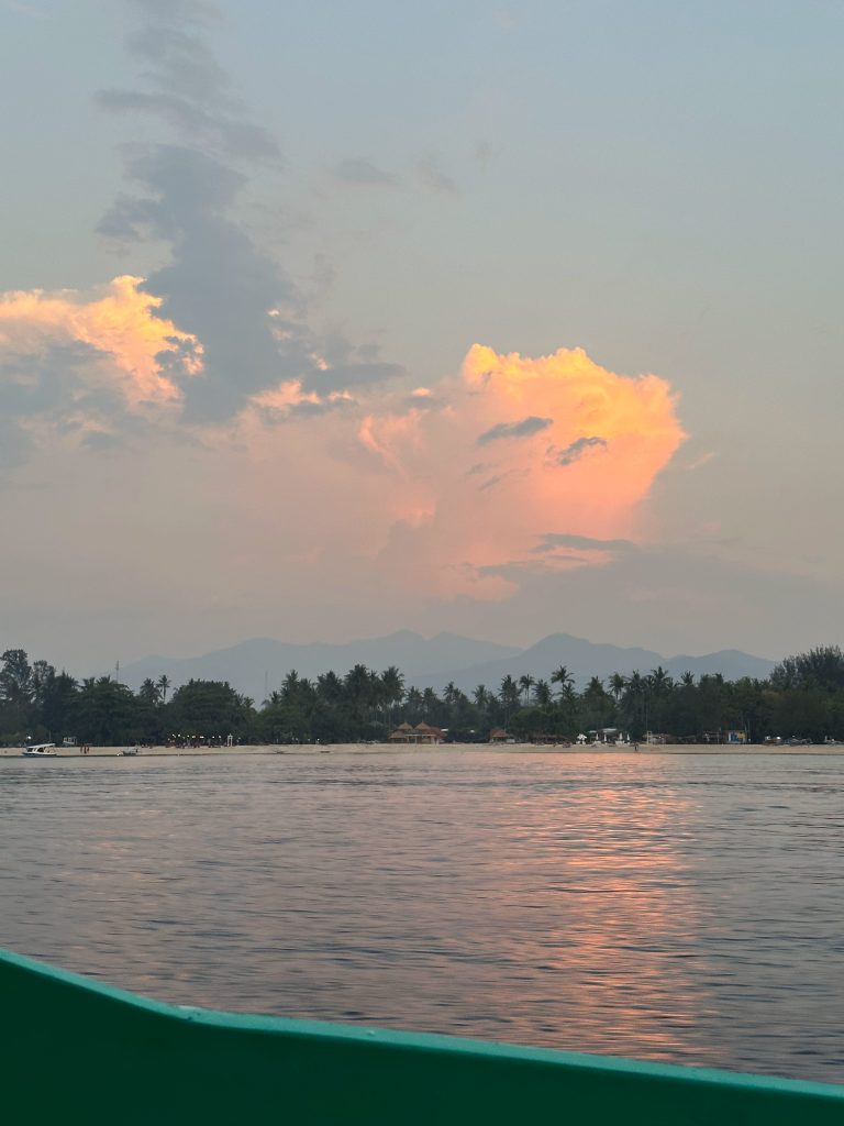 Warm orange sunset clouds over the coast of Gili Air and Gili Meno with views toward the mountains in the back. 