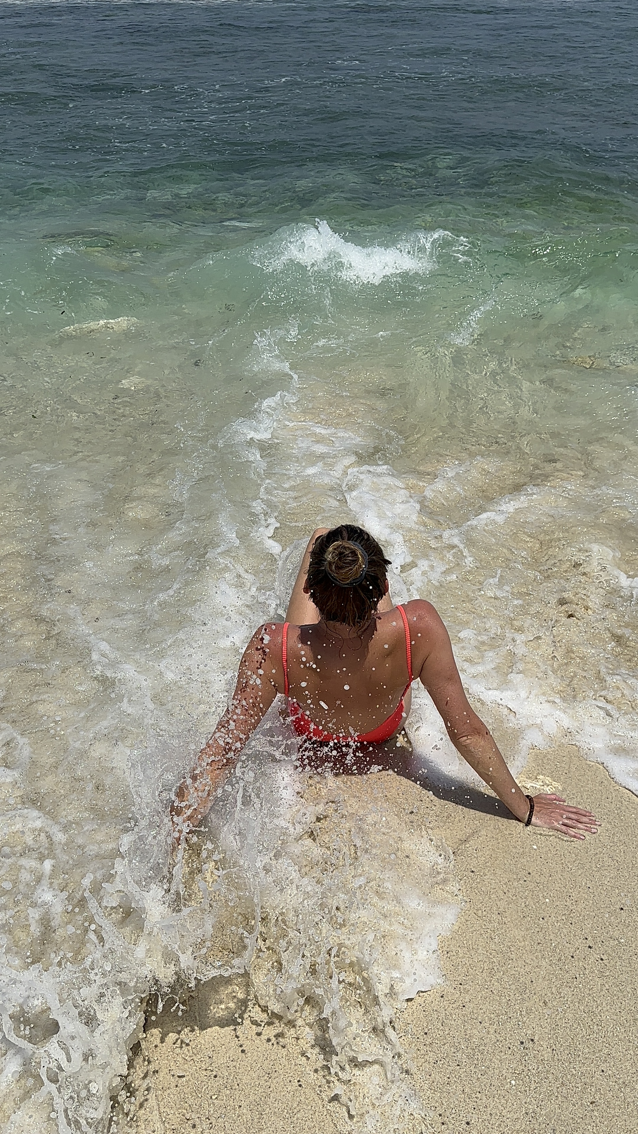 Woman sitting in the waves on a sandy beach in Nusa Lembongan, Indonesia