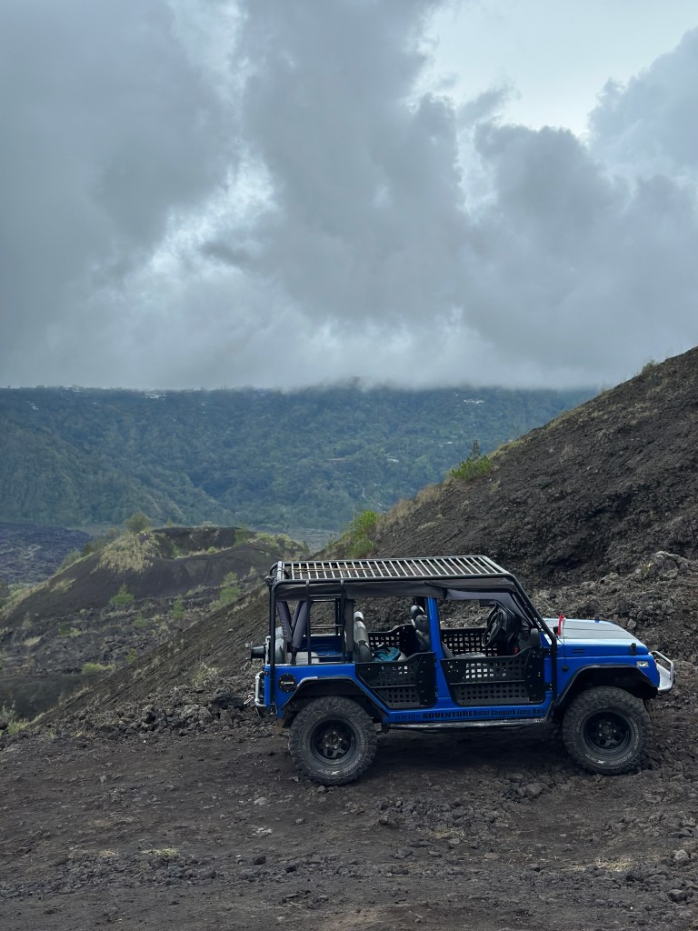 Blue jeep driving through the black lava fields of Mount Batur in Kintamani