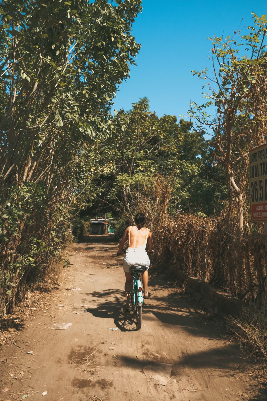 Woman cycling along a quiet dirt road surrounded by trees in Lombok, Indonesia