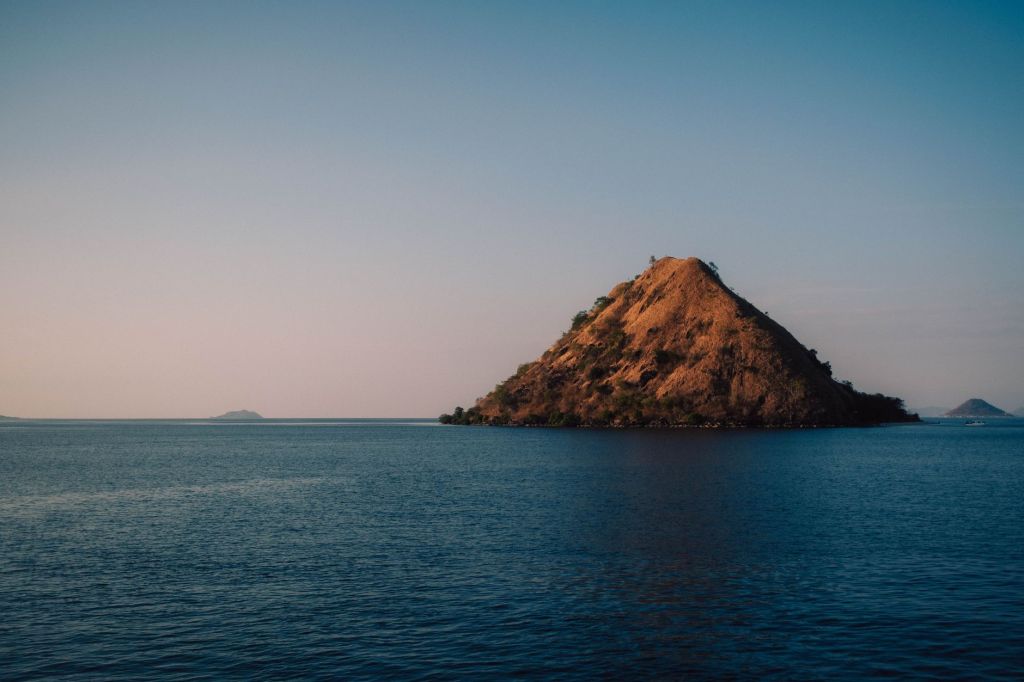 Dry golden island rising from blue water at sunset in Komodo National Park.
