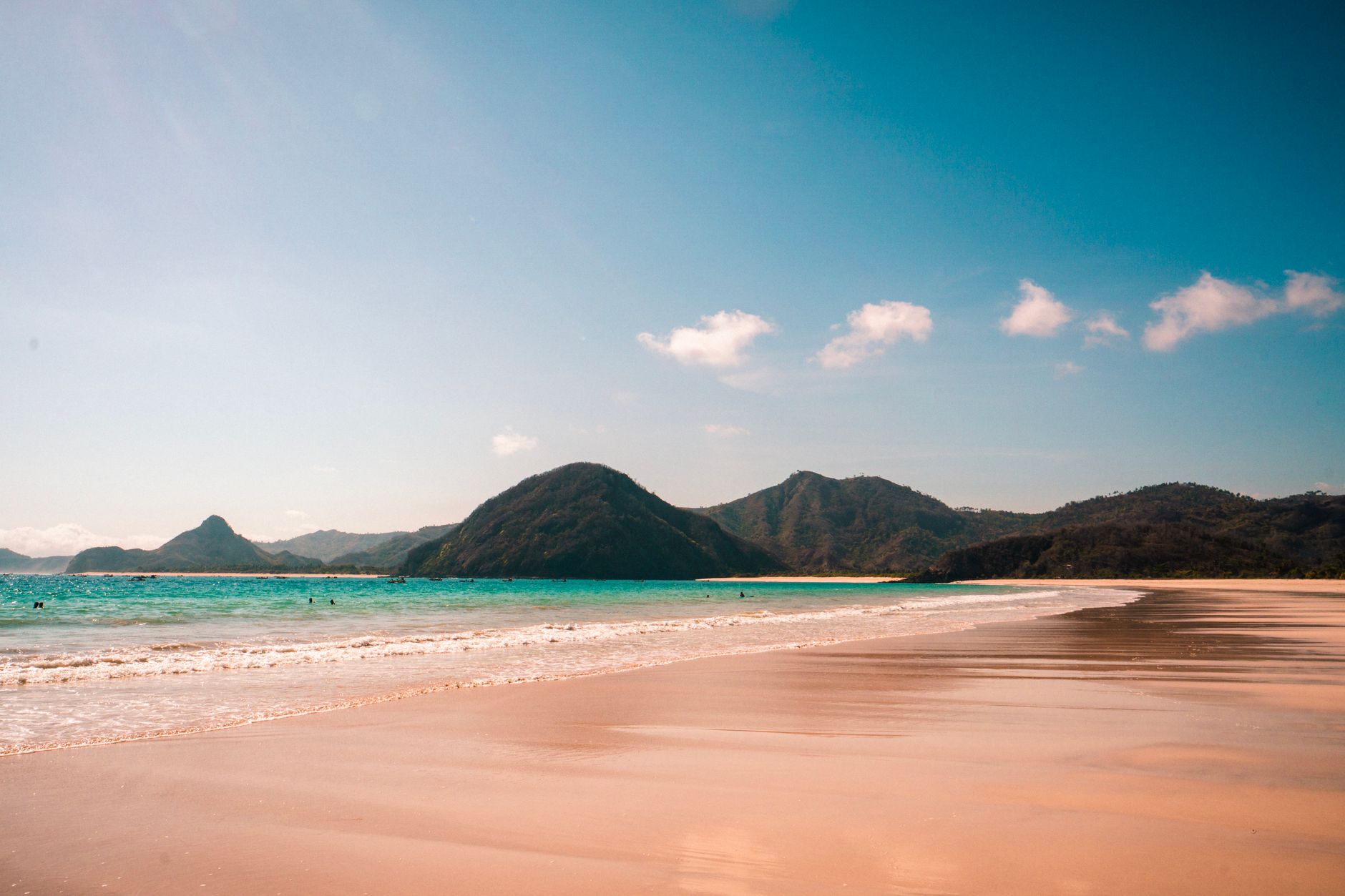 Pink-sand beach with turquoise water and green hills along the coast of Lombok, Indonesia