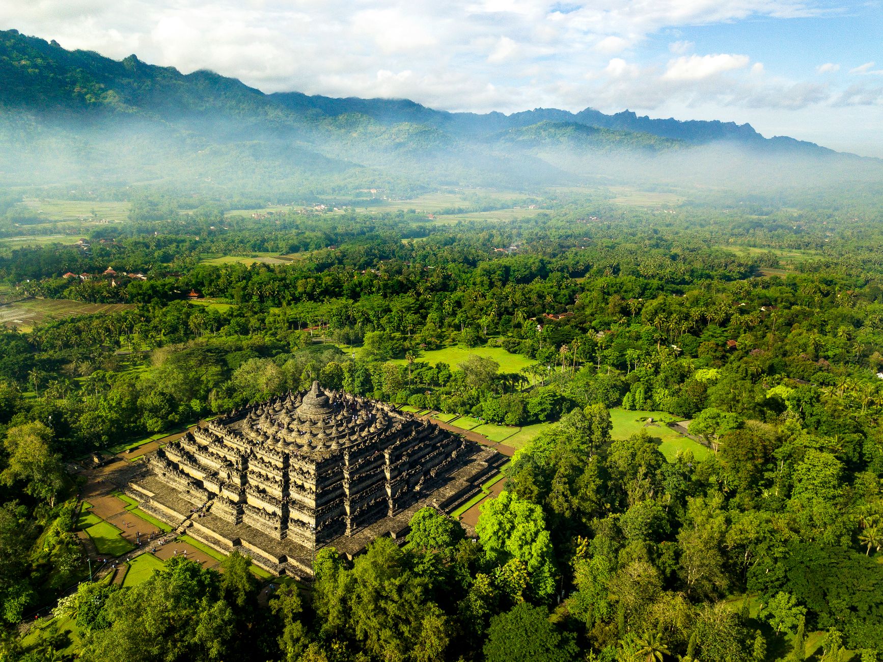Aerial view of Borobudur Temple surrounded by green forest and hills in Central Java