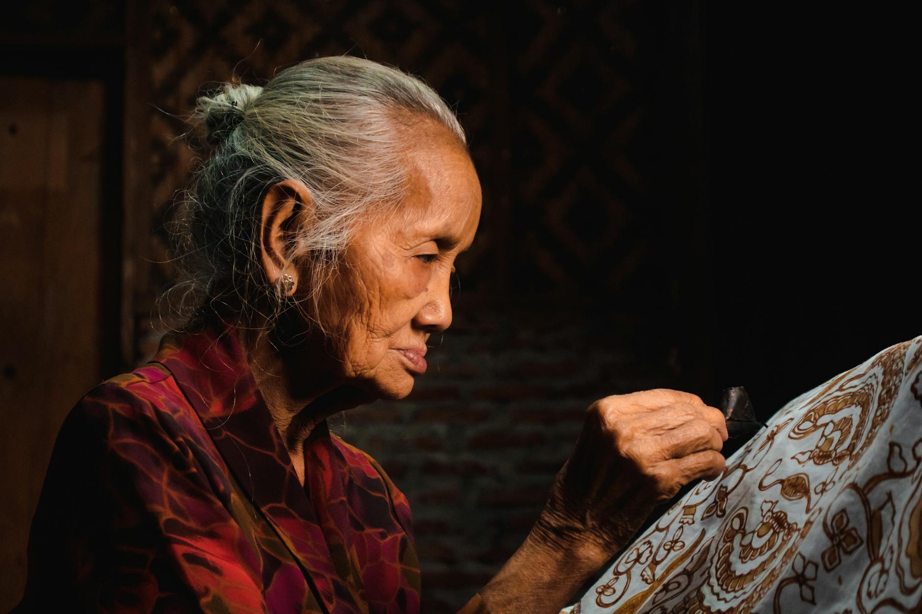Elderly woman making batik textile by hand in Yogyakarta