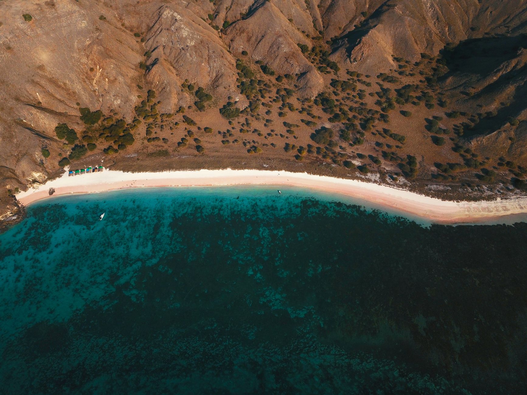 Aerial view of Pink Beach beside dark coral reef and turquoise water in Komodo National Park.
