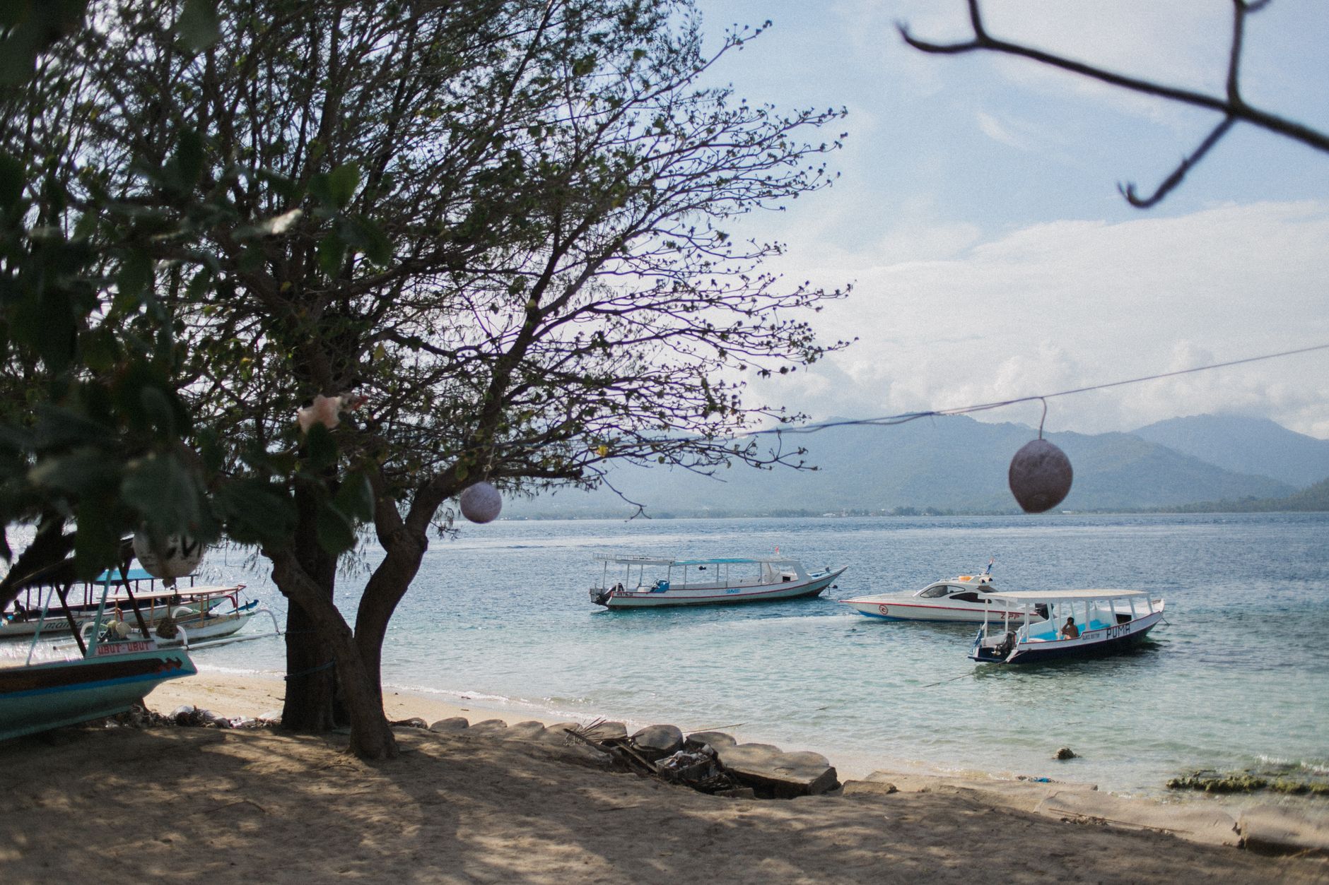 Boats anchored off Gili Air with calm sea, island trees, and mountain views near Lombok