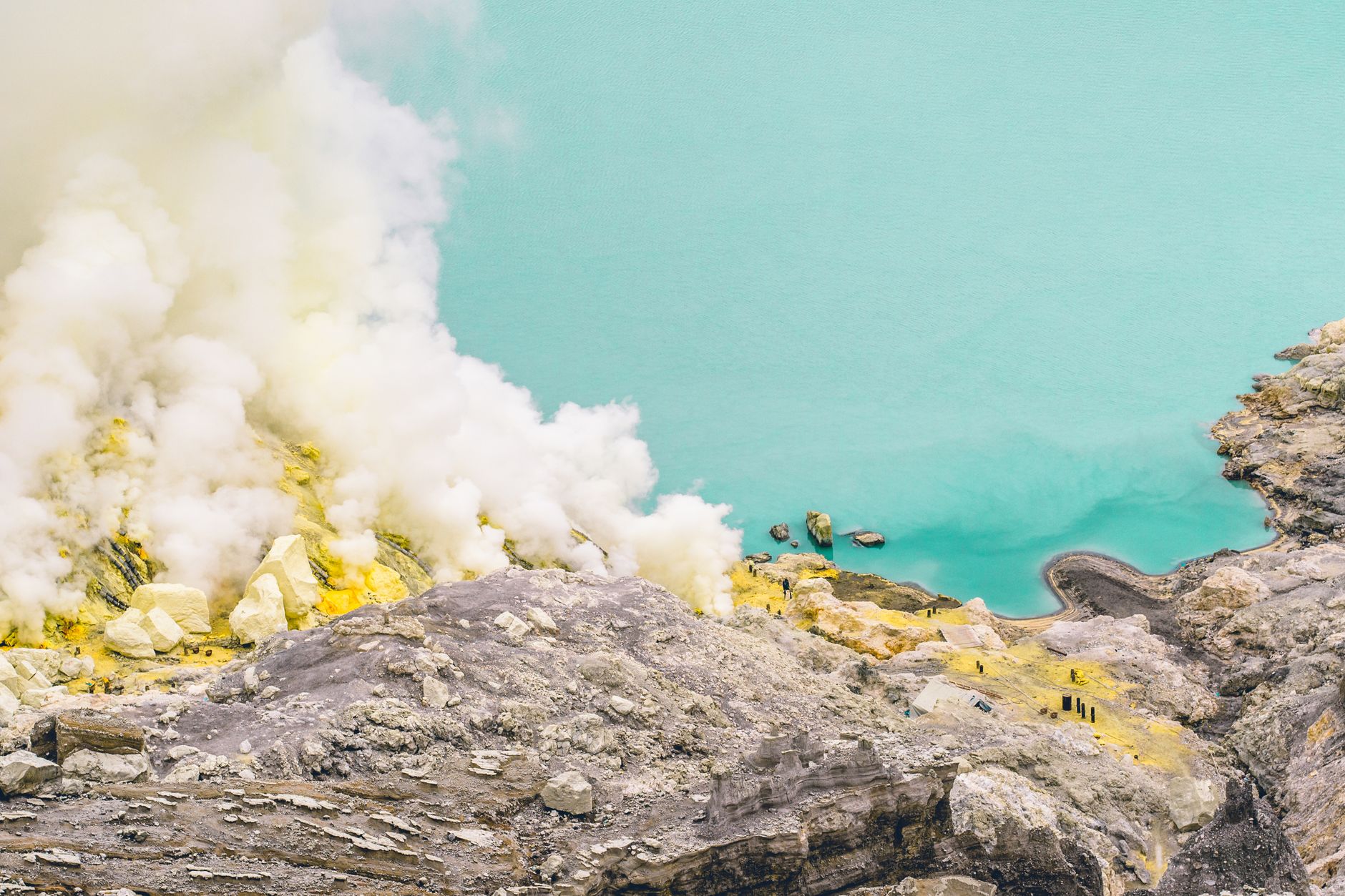 Sulfur smoke rising beside the turquoise crater lake of Mount Ijen in East Java