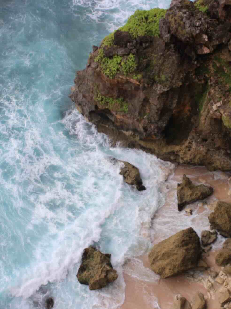 Turquoise waves crashing onto a small beach cove below the cliffs in Uluwatu, Bali