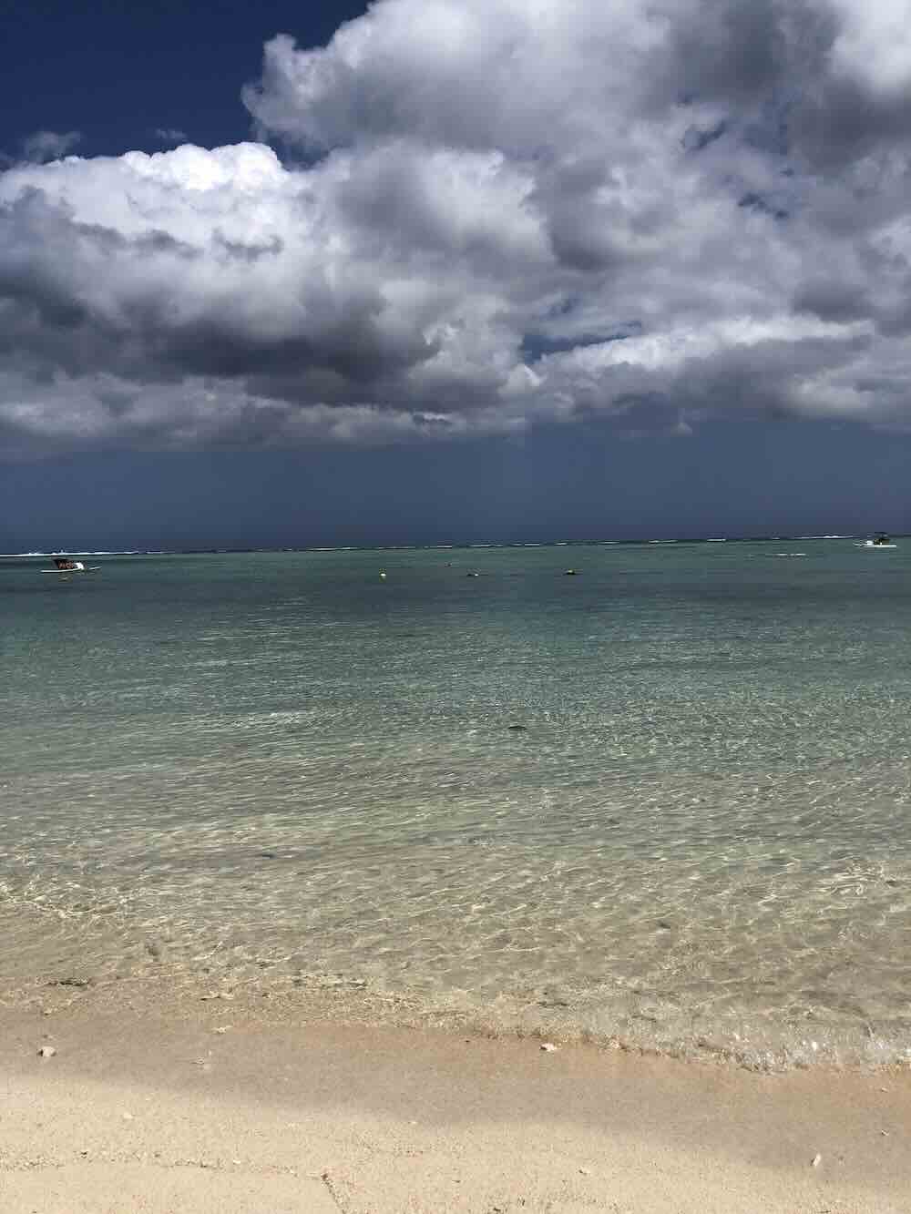 Clear shallow lagoon with storm clouds gathering over Flic en Flac Beach in Mauritius.