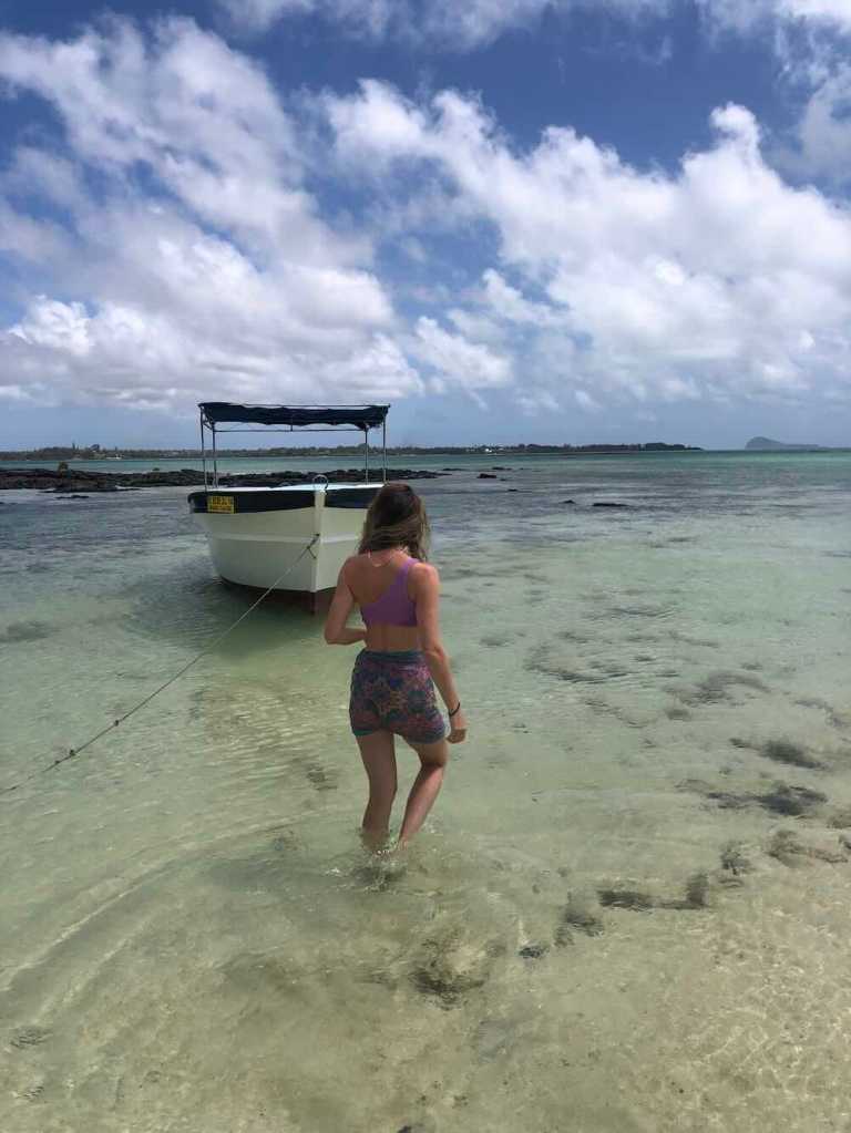 Woman walking through the shallow lagoon towards a small boat at Île aux Cerfs, Mauritius.