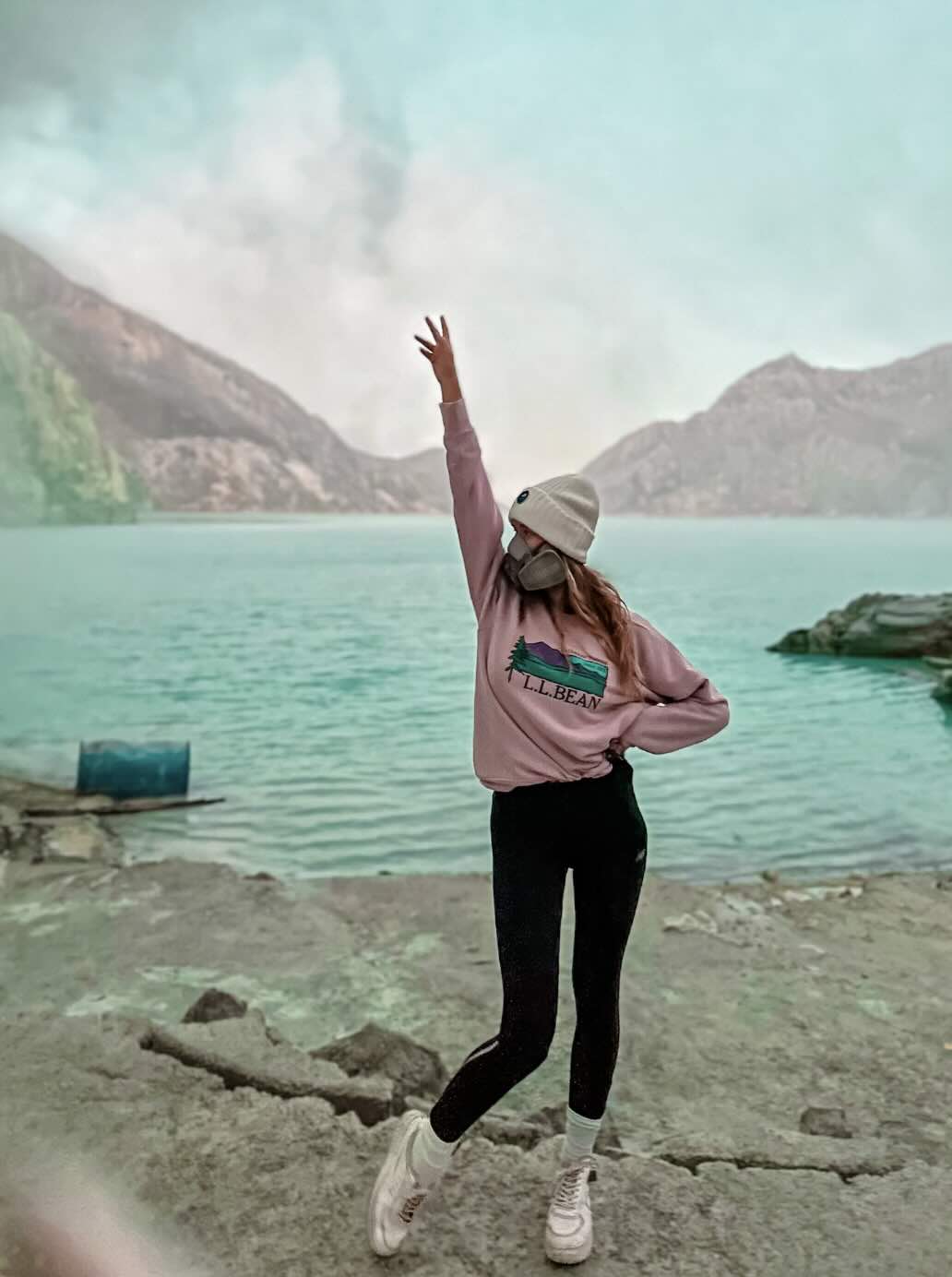 Traveler standing near the blue crater lake and sulfur smoke at Kawah Ijen