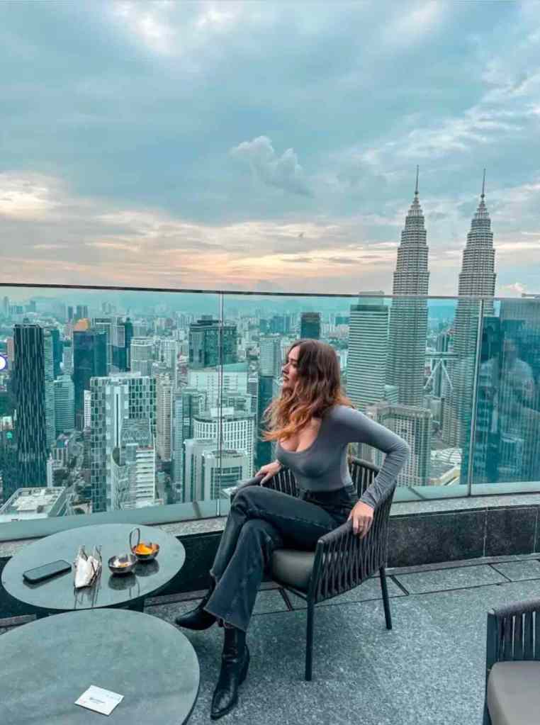 Travel creator sitting on a rooftop terrace overlooking the Kuala Lumpur skyline and Petronas Towers