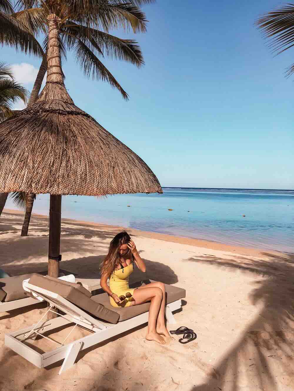 Woman relaxing beneath a beach umbrella on Le Morne Beach with turquoise water in Mauritius.