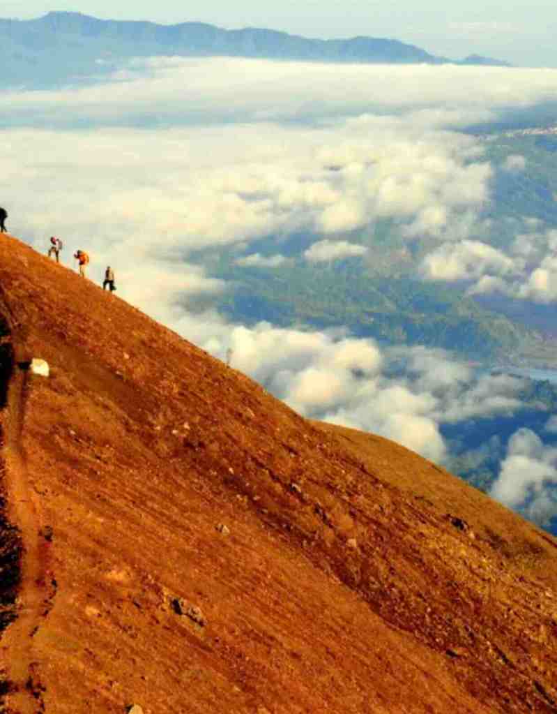 Hikers climbing the steep volcanic slope of Mount Agung above the clouds