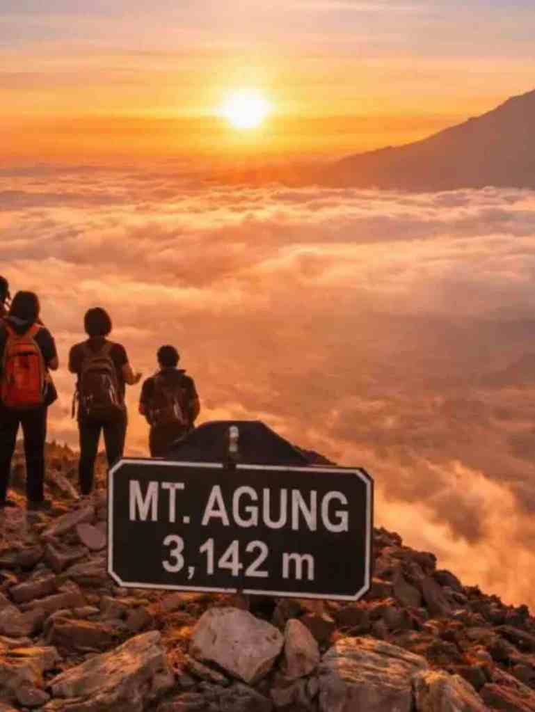 Hikers standing by the Mount Agung 3142 meter summit sign at sunrise