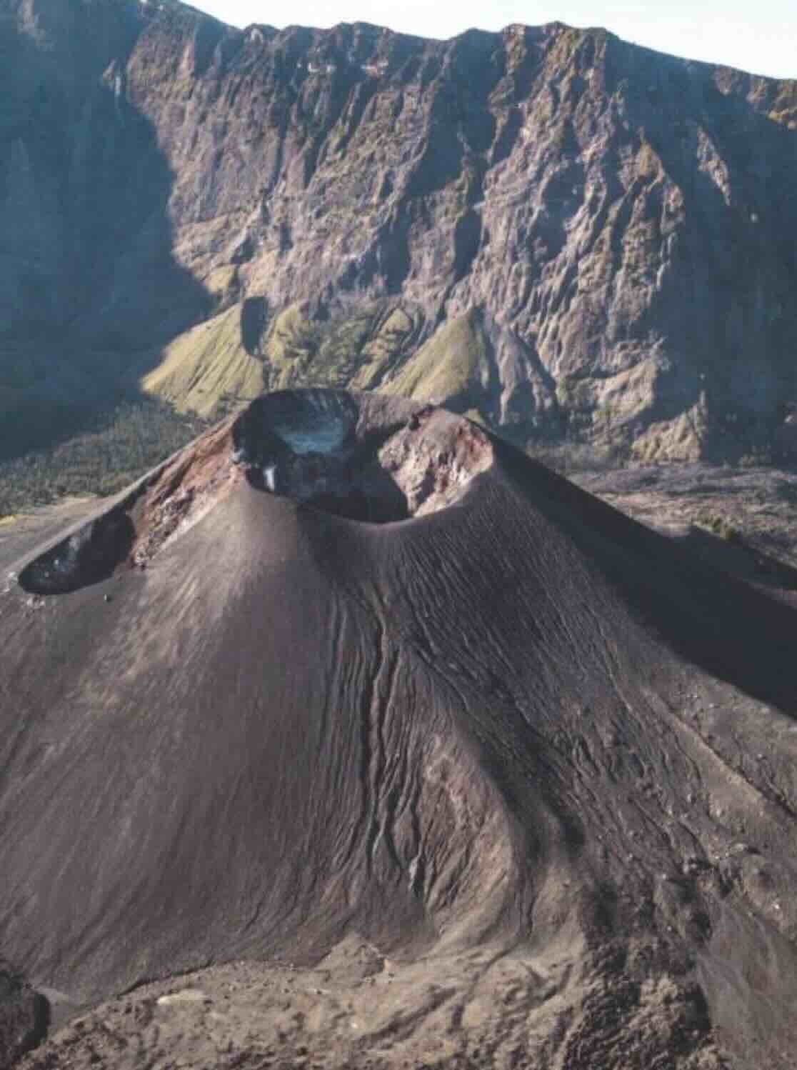 Volcanic cone inside Mount Rinjani crater with steep crater walls behind it