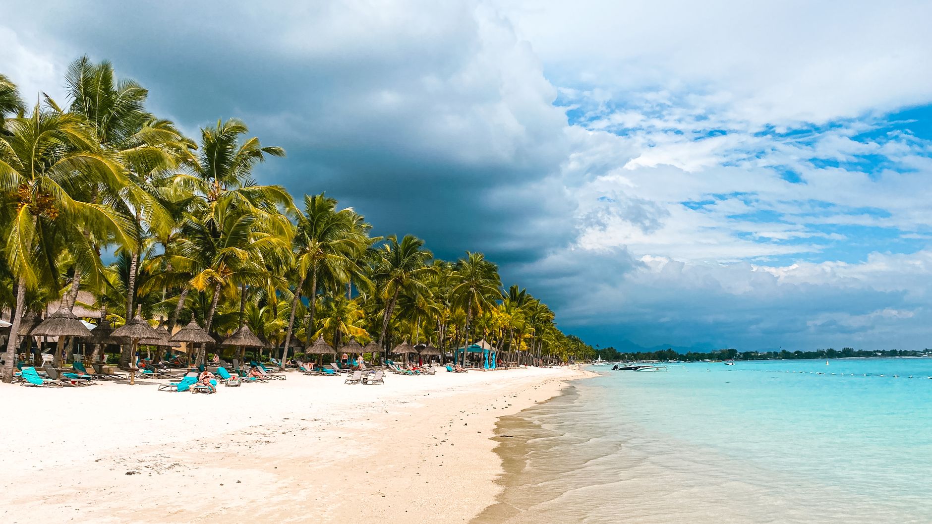 Palm-lined white sand beach at Flic en Flac with turquoise water and dramatic clouds in Mauritius.