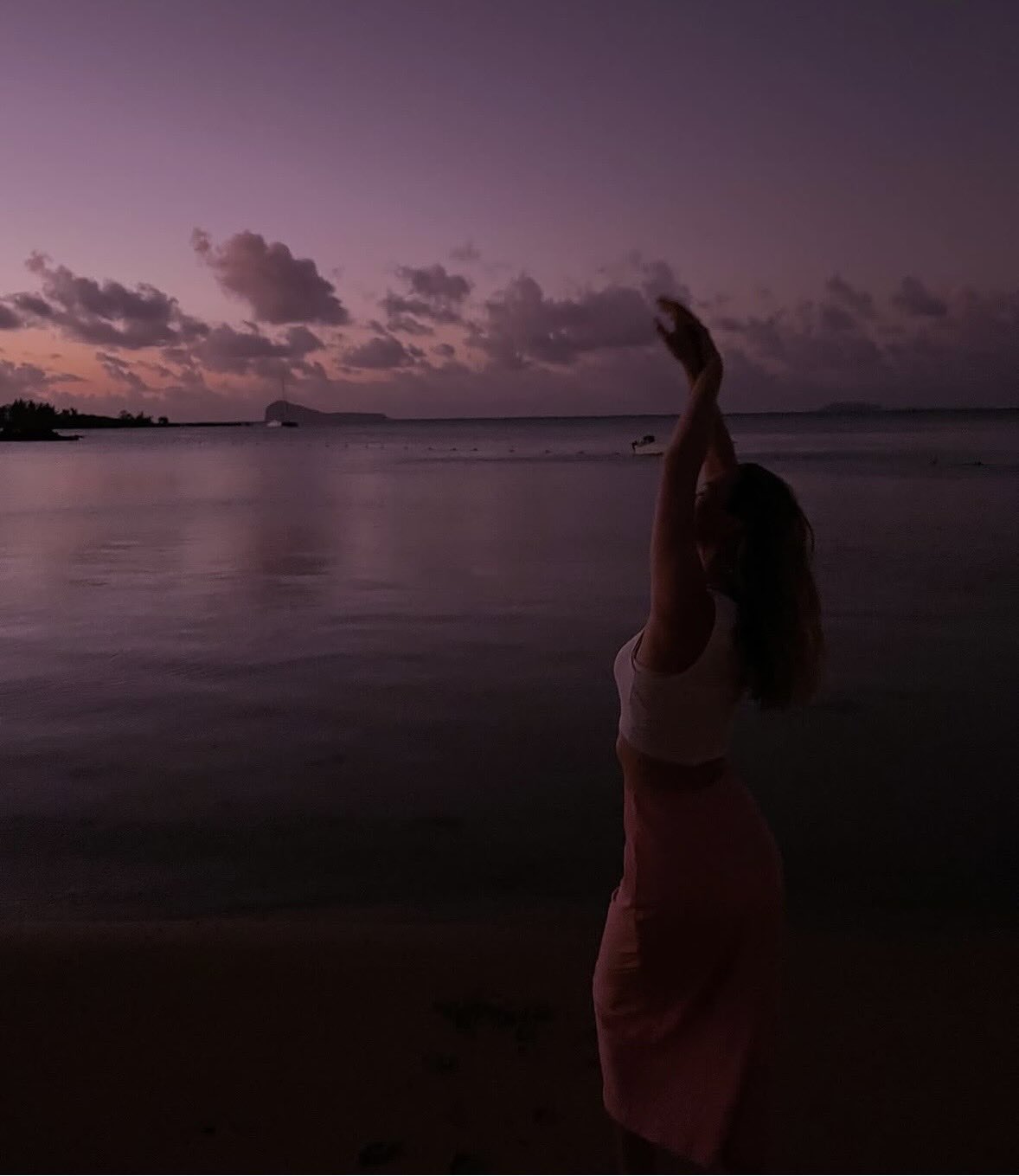 Woman watching the pink sunset over the calm lagoon at Le Morne Beach in Mauritius.