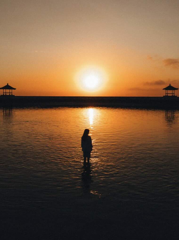 Person standing in calm water during sunrise at Sanur Beach in Bali