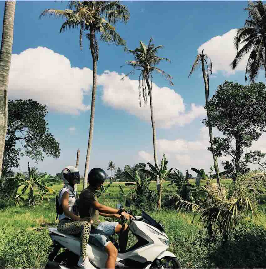 Travelers riding a scooter through palm trees along the Amed coastline in Bali