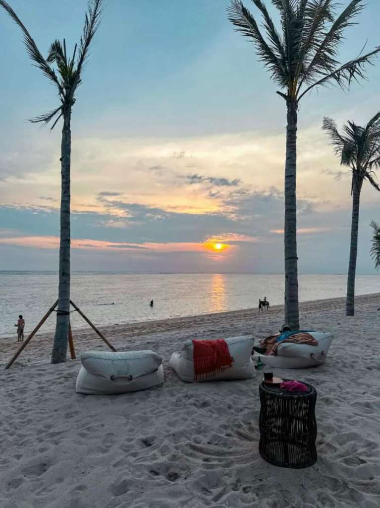 beach club in West Sumba at sunset, with lounge seating, palm trees, and ocean views.