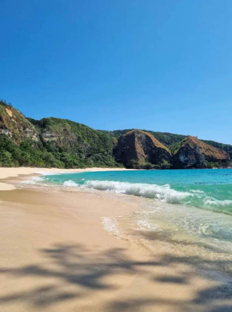 Turquoise beach in South Sumba with clear waves, golden sand, and dramatic coastal cliffs.
