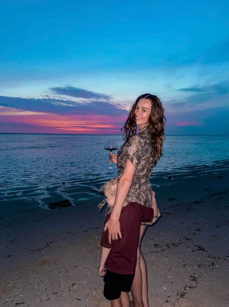 Traveler standing on a West Sumba beach at sunset, with colorful skies and calm coastal views.