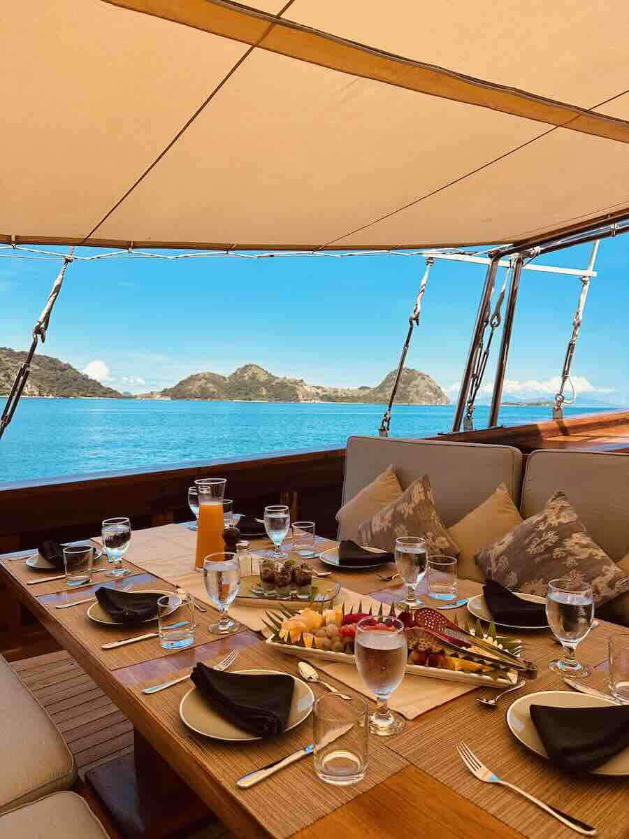 Breakfast table set on the outdoor deck of a Komodo liveaboard with island views.