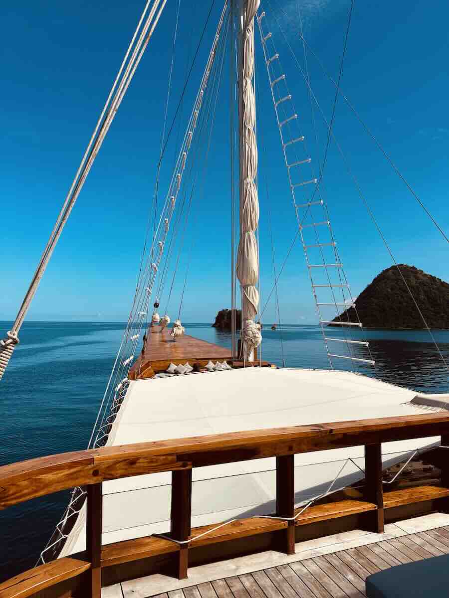 Wooden deck of the MAJ Oceanic liveaboard overlooking blue water and Komodo islands.