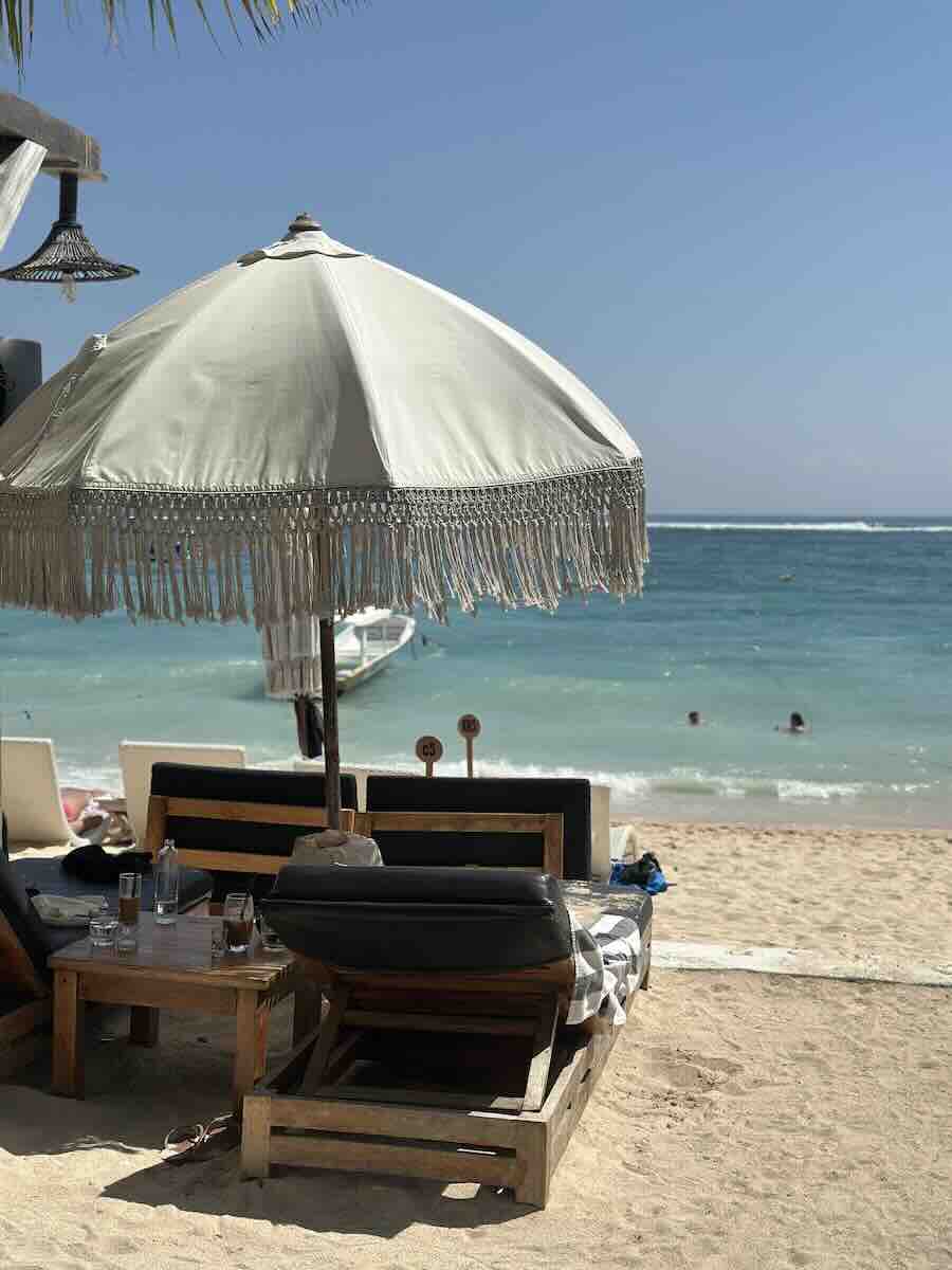 Beachfront loungers beneath a large umbrella overlooking turquoise water in Nusa Ceningan, Bali.