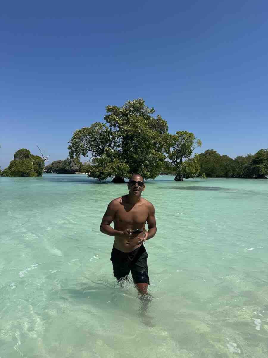 Man walking through shallow crystal-clear turquoise water surrounded by mangroves near Hakara in Rote.