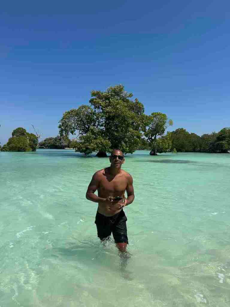 Man walking through shallow crystal-clear turquoise water surrounded by mangroves near Hakara in Rote.