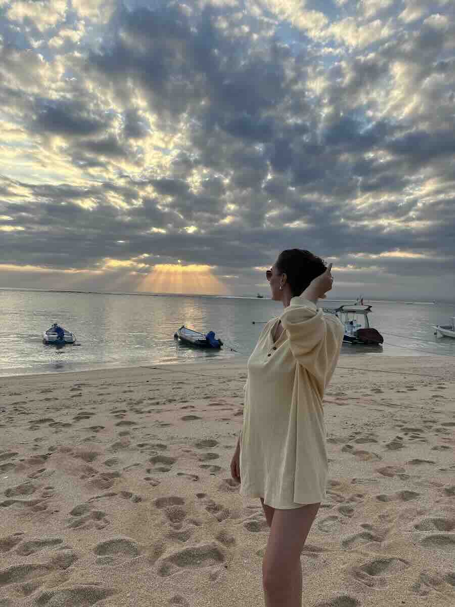 Traveler watching sunset from a sandy beach with small boats anchored offshore in Nusa Lembongan.