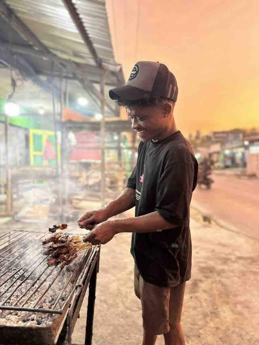 Local vendor grilling sate at a roadside food stall in Mokdale, Rote Island