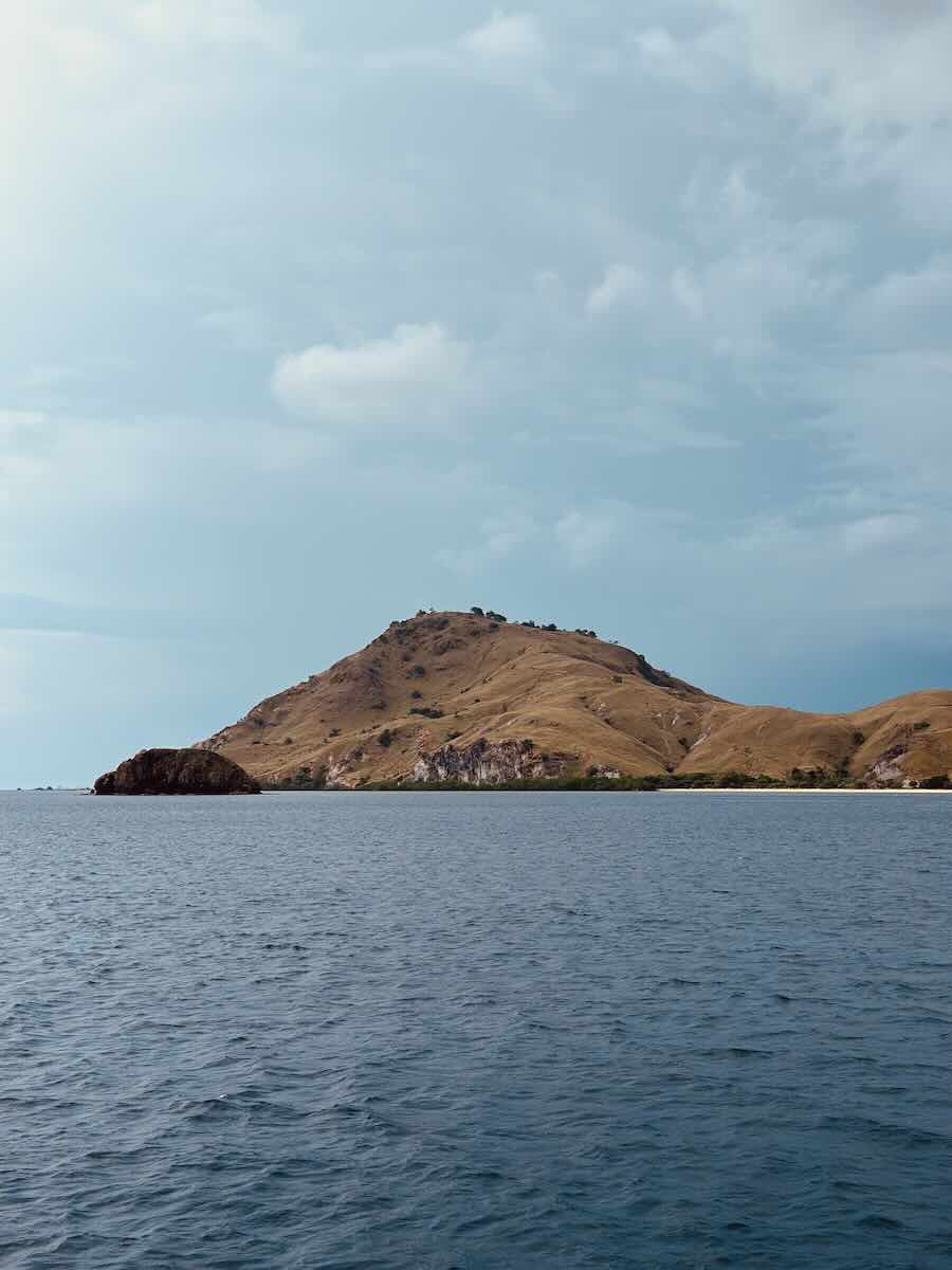 Dry hills of Sebayur Island rising from calm blue water in Komodo National Park.